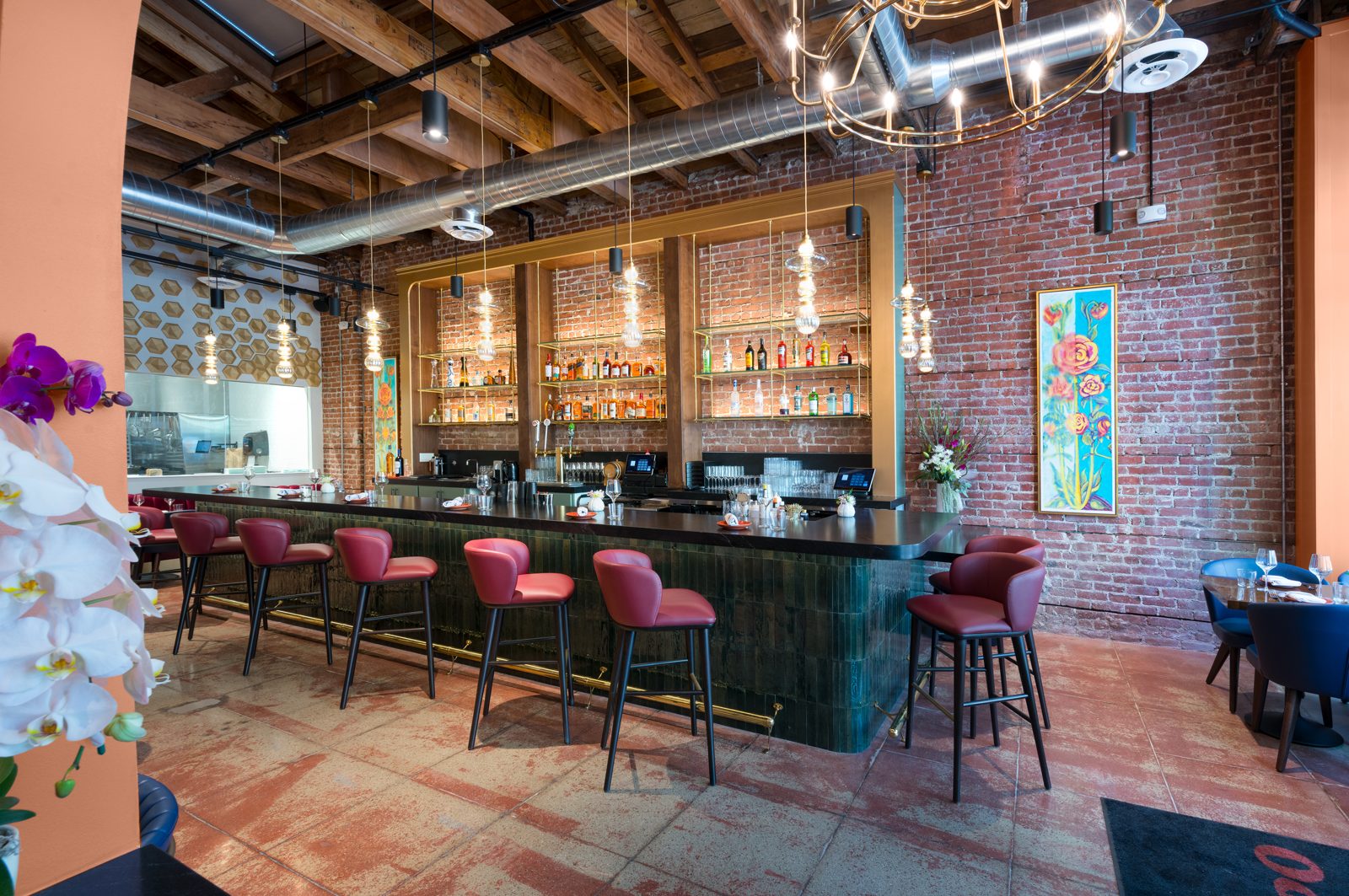 The bar at L Campo: red leather stools along a dark green tiled bar, brass shelves of bottles against exposed brick, a brass chandelier above.